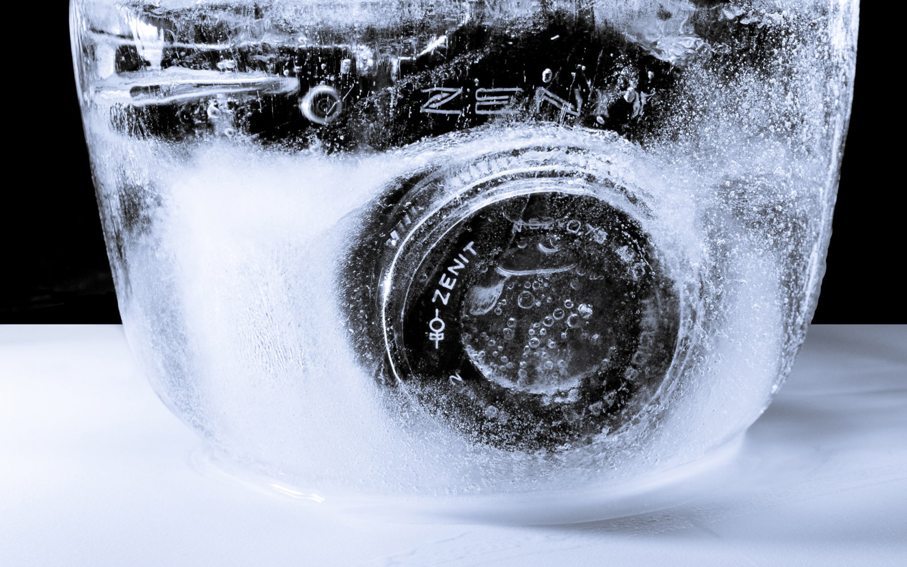 A vintage Zenit camera frozen in a block of ice, with air bubbles trapped around the lens. The camera's brand name is visible through the ice