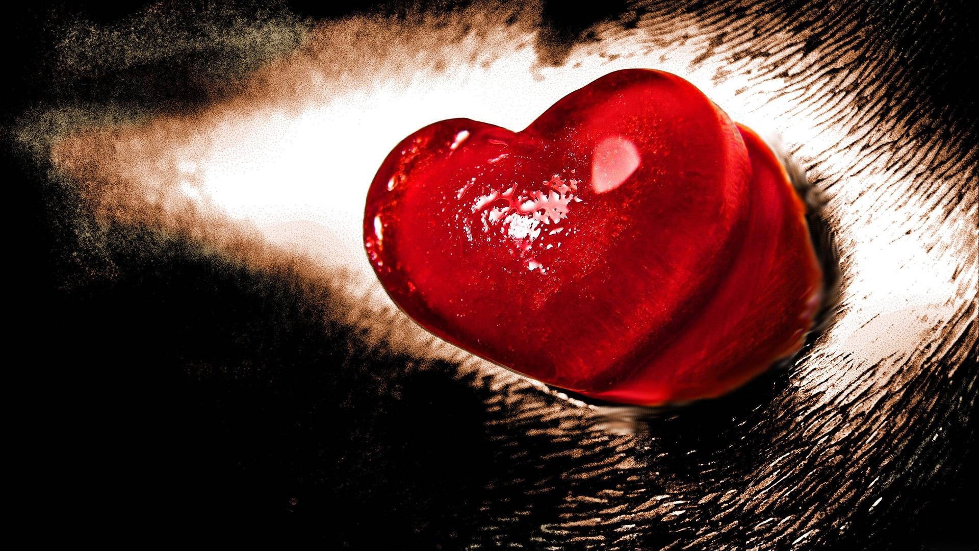 A glistening red heart-shaped candy or gemstone on a textured, dark background, evoking feelings of love, passion, and sweetness