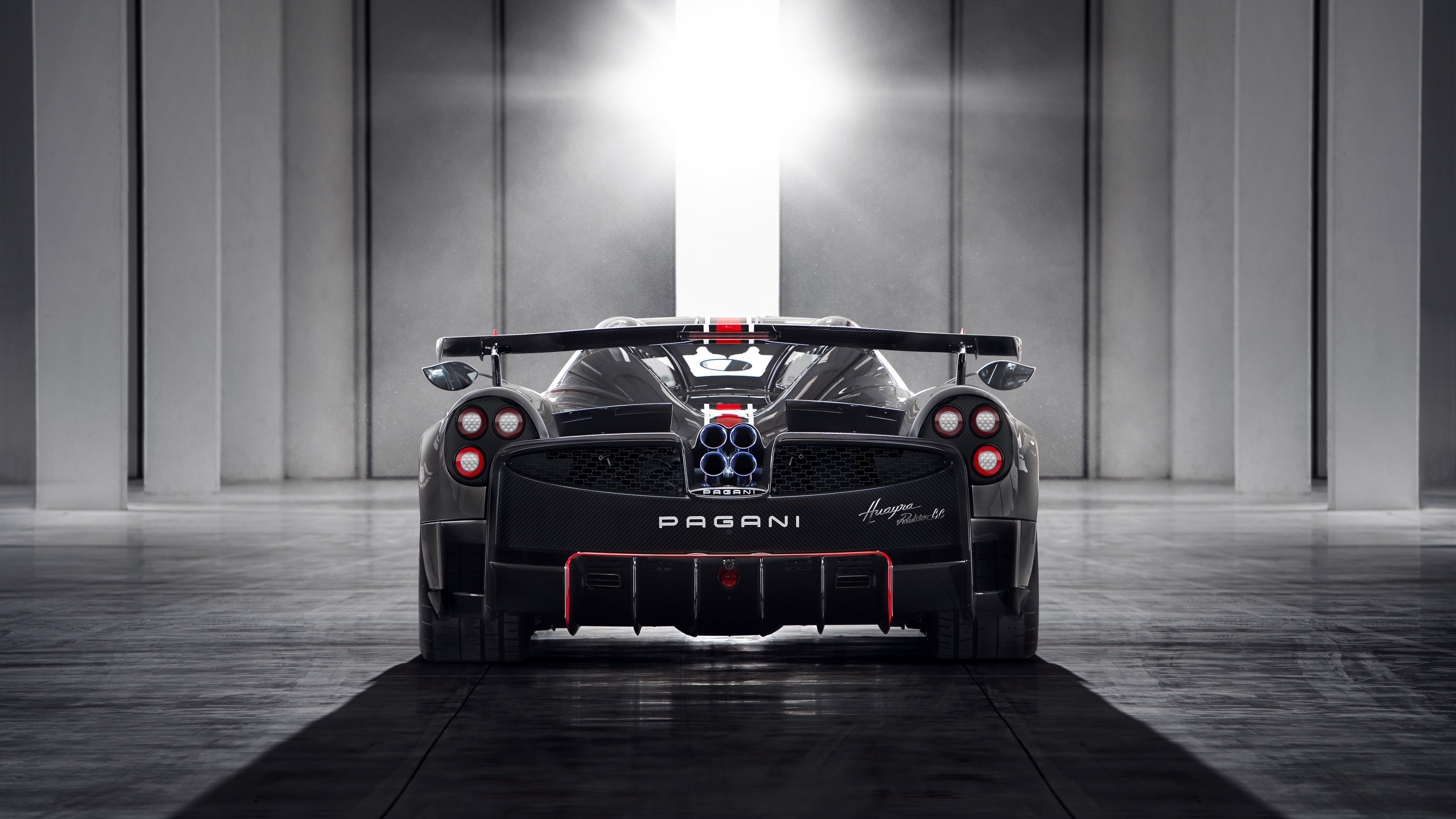 Rear view of a Pagani Huayra BC in a modern garage, showcasing its unique quad exhaust and aerodynamic design
