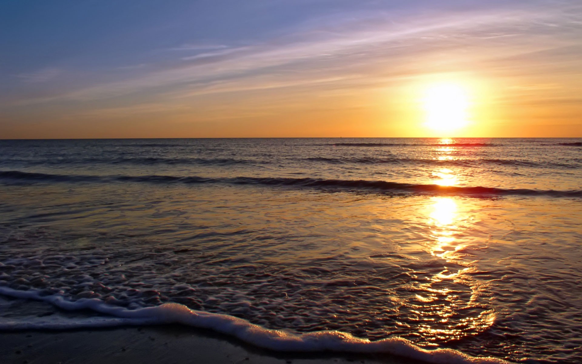 Sunset over a calm ocean with gentle waves lapping at the shore