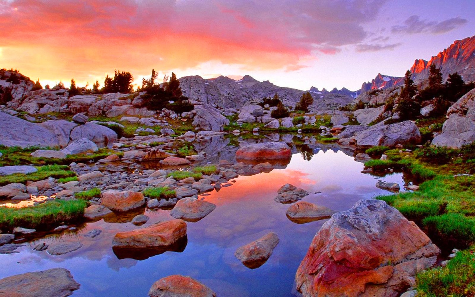 A breathtaking sunset reflected in a tranquil alpine lake, surrounded by colorful rocks and lush vegetation