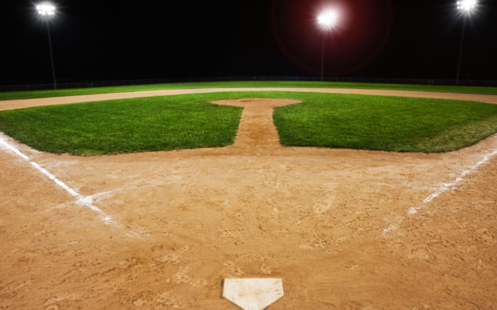 A baseball field at night, lit by stadium lights, with the focus on home plate