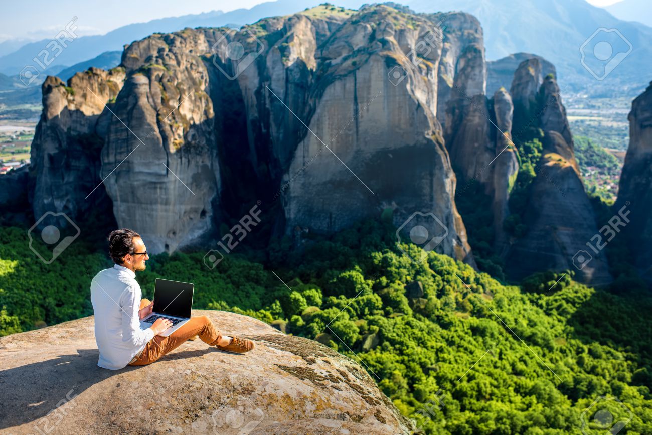 Well Dressed Man Working With Laptop Sitting On The Rocky Mountain