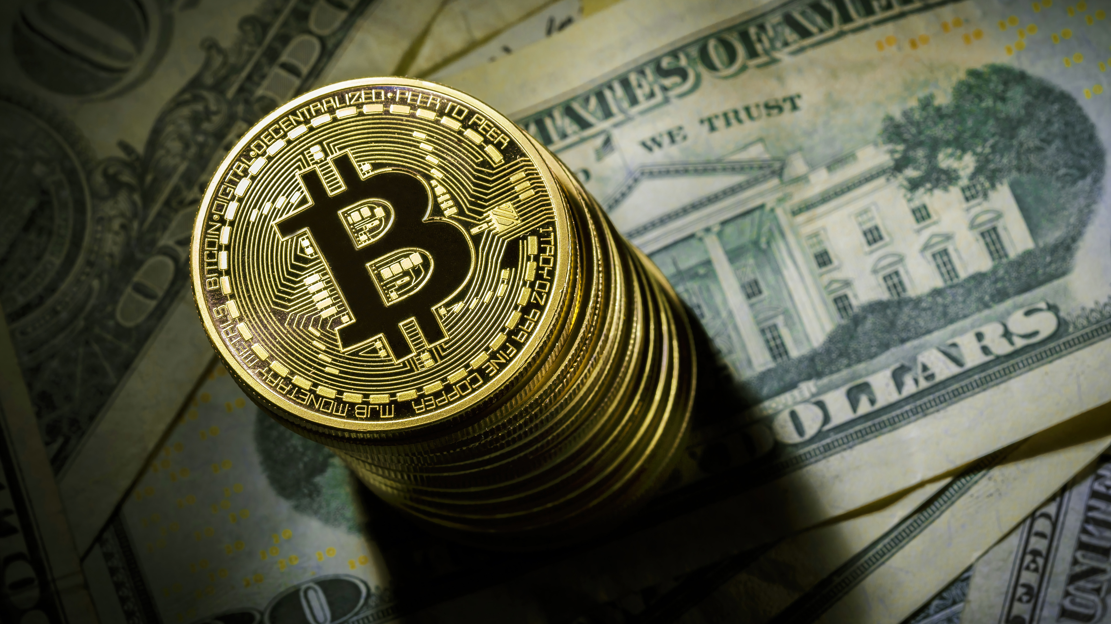 A stack of shiny gold Bitcoin coins on a bed of US dollar bills, symbolizing the intersection of cryptocurrency and traditional finance