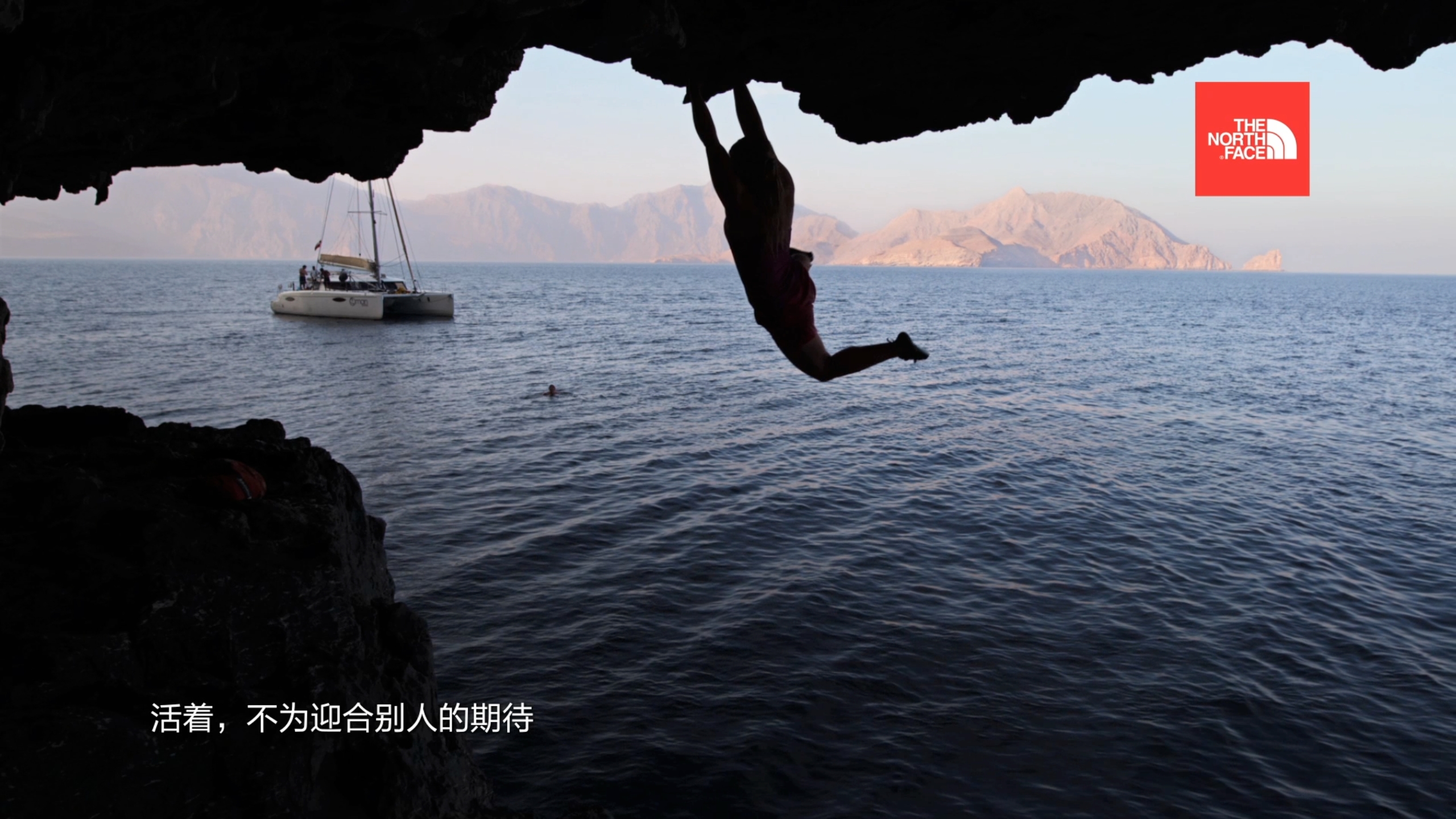 A climber hangs from a cliff overlooking the ocean, wearing The North Face apparel