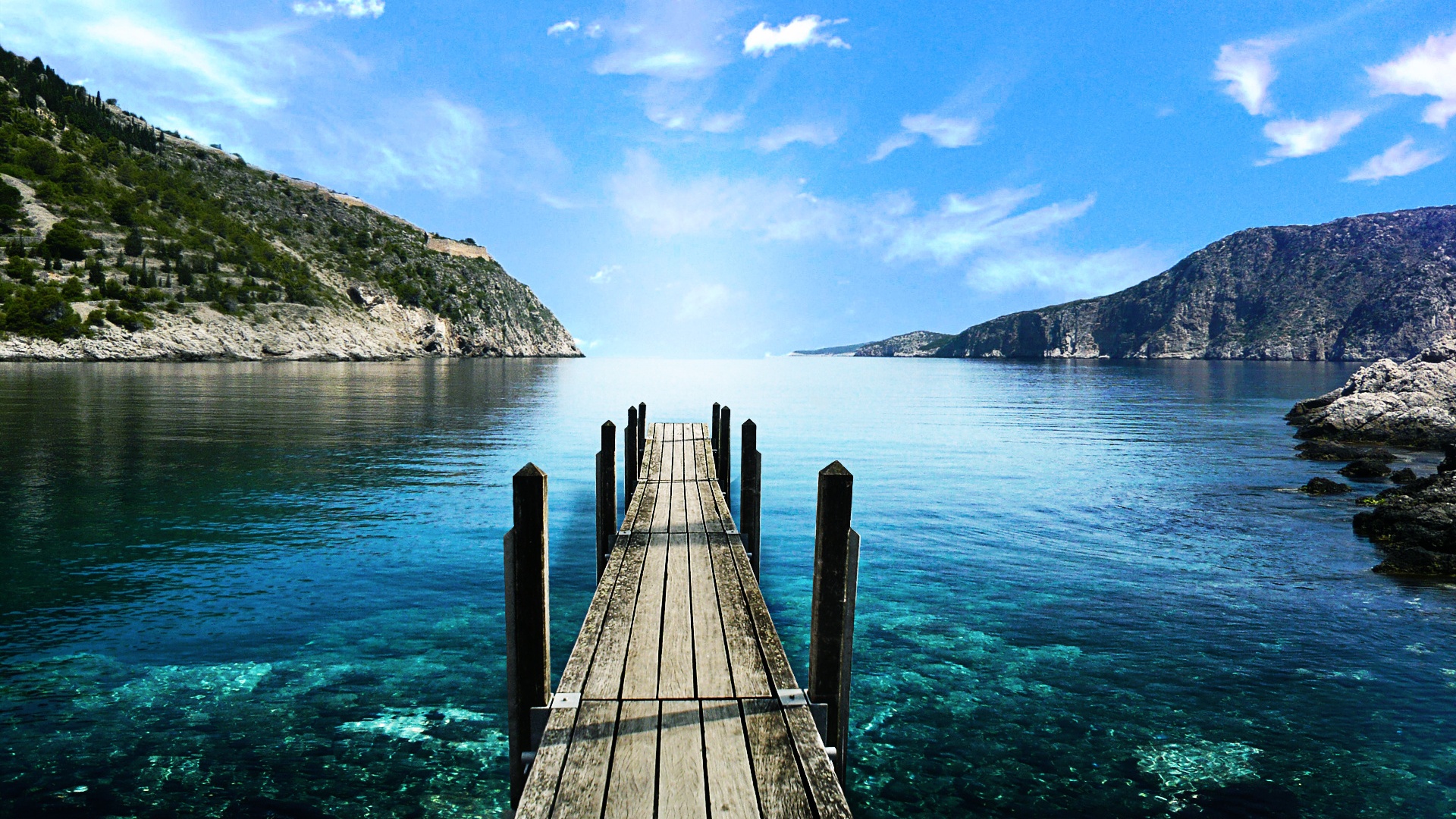 Scenic view of a wooden pier extending into crystal-clear turquoise water, surrounded by lush green hills and a vibrant blue sky with fluffy white clouds. Perfect wallpaper for computer