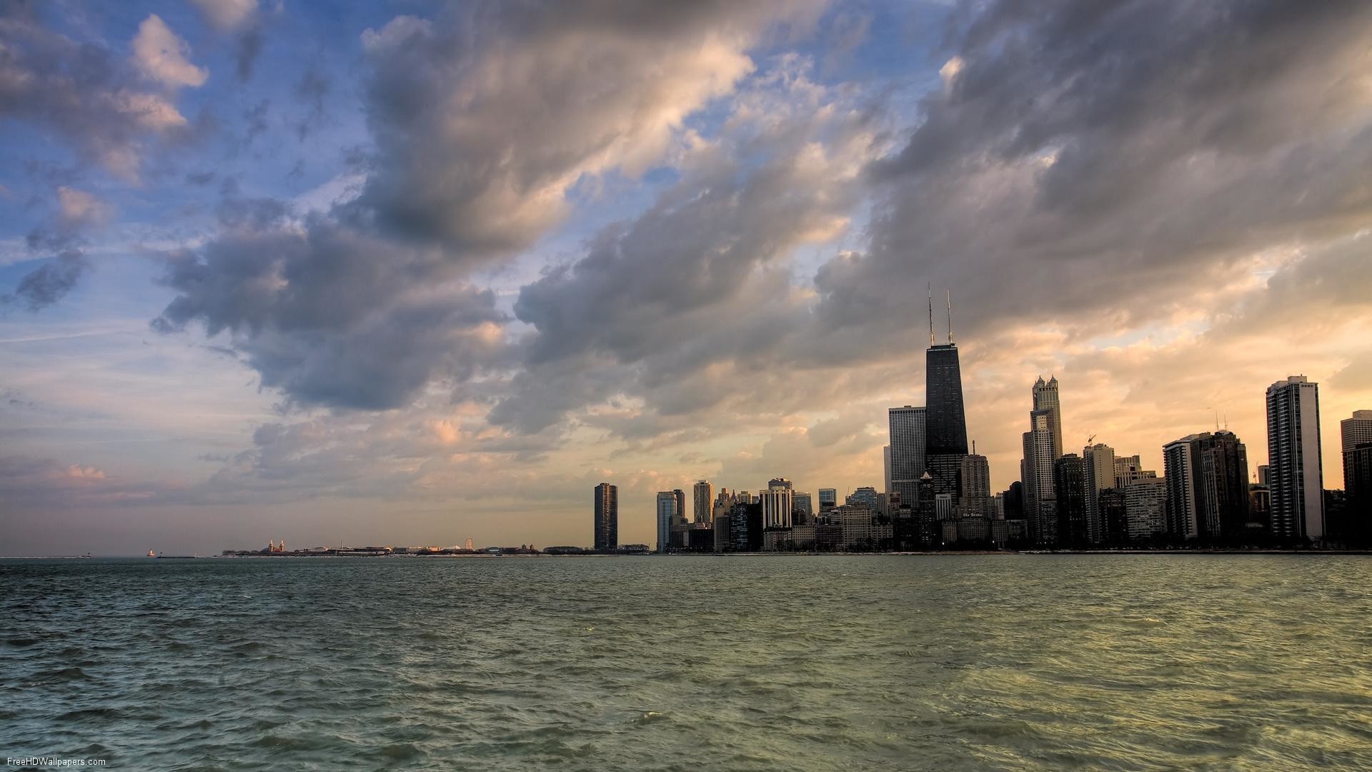 Dramatic sunset over the Chicago skyline, with the city's iconic skyscrapers silhouetted against the colorful sky and reflecting in the calm waters of Lake Michigan