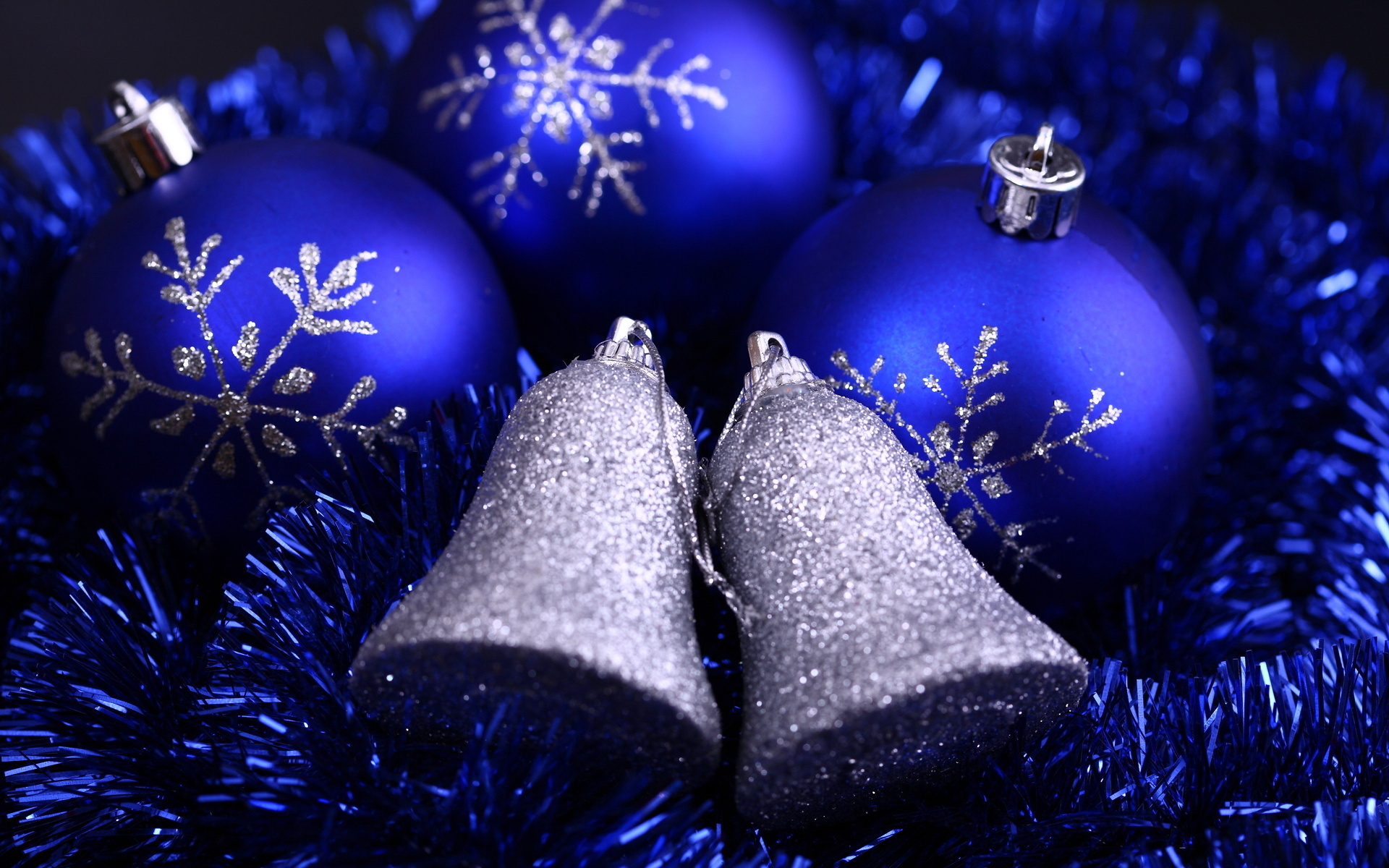 Close-up of blue Christmas ornaments and silver bells nestled in shimmering blue tinsel, evoking a festive holiday spirit