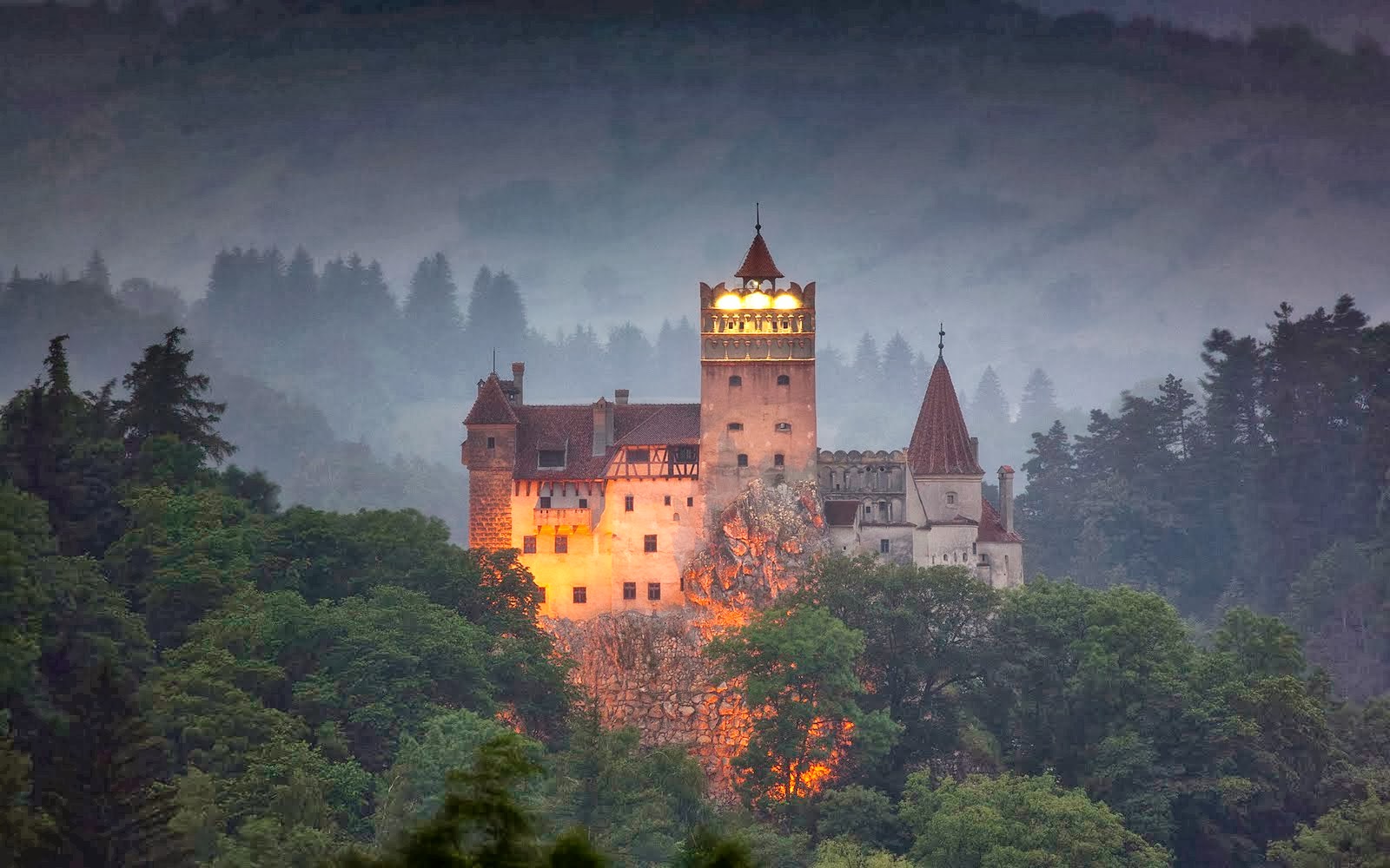 Bran Castle, also known as Dracula's Castle, illuminated at dusk amidst the misty Carpathian Mountains in Transylvania, Romania