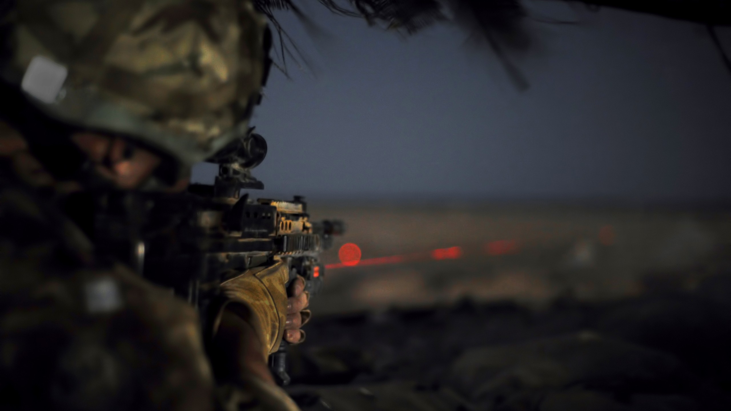 A soldier aims a rifle fitted with a laser sight in the darkness, highlighting the precision and intensity of military operations