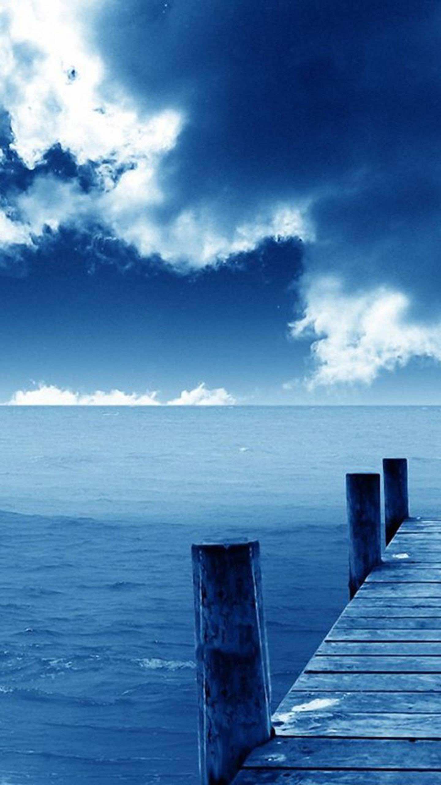 Serene blue ocean landscape with a wooden pier and cloudy sky, perfect for a cool phone wallpaper