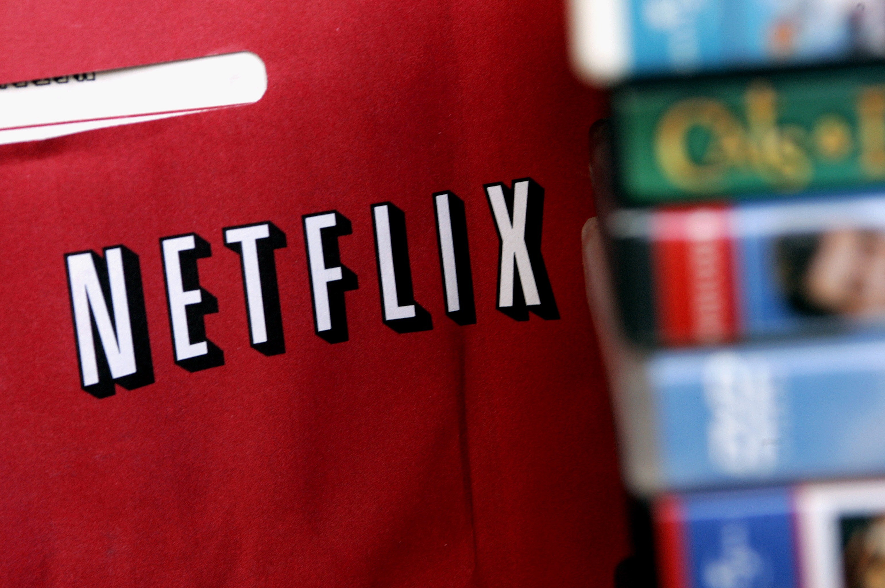 Close-up of a red Netflix envelope with a stack of DVDs in the background, highlighting the transition from physical media to streaming