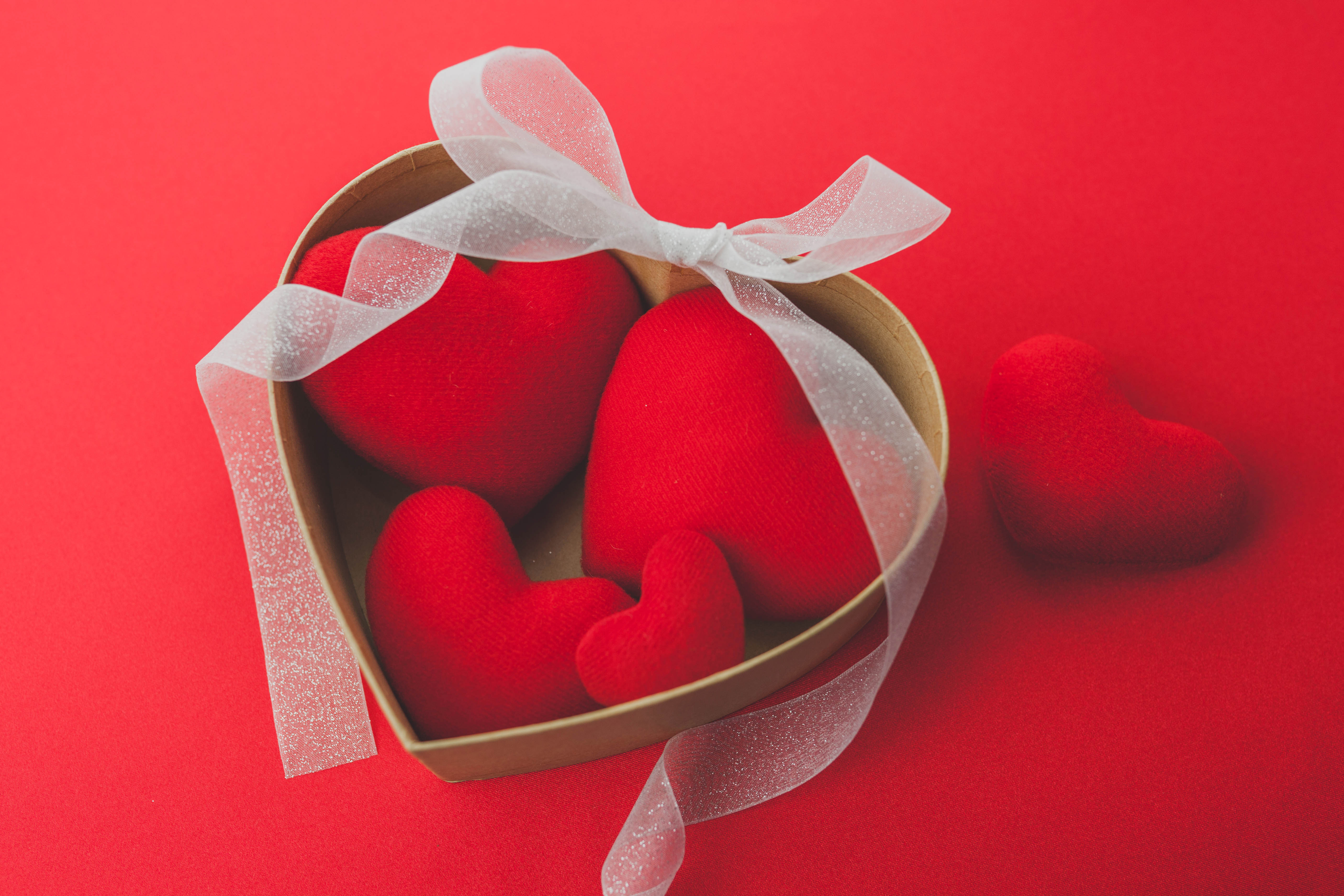 Red heart-shaped decorations in a heart-shaped box with a white ribbon, against a red background, perfect for Valentine's Day