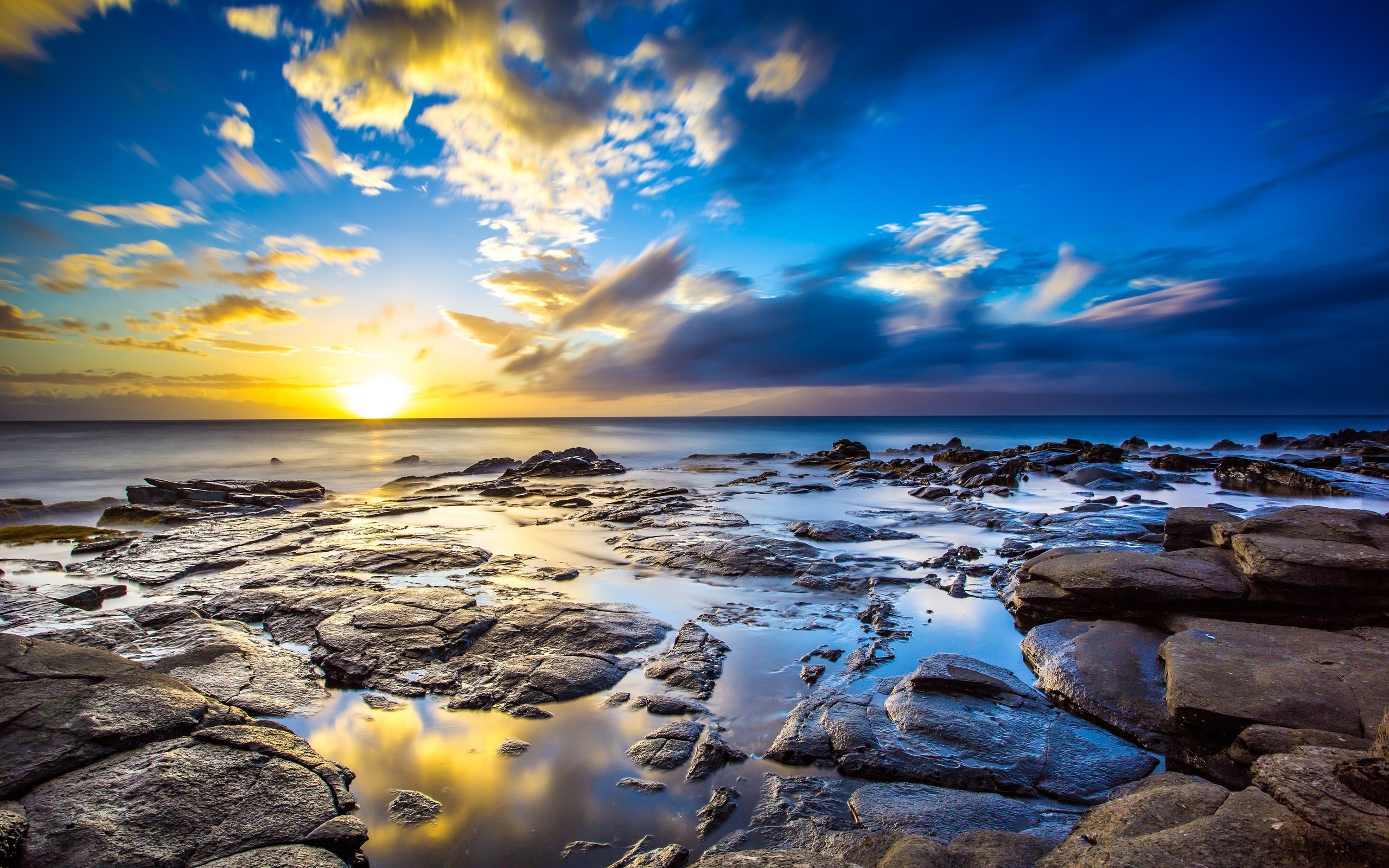 Stunning 4K wallpaper of a vibrant sunset over a rocky coastline, with the colorful sky reflected in the tide pools