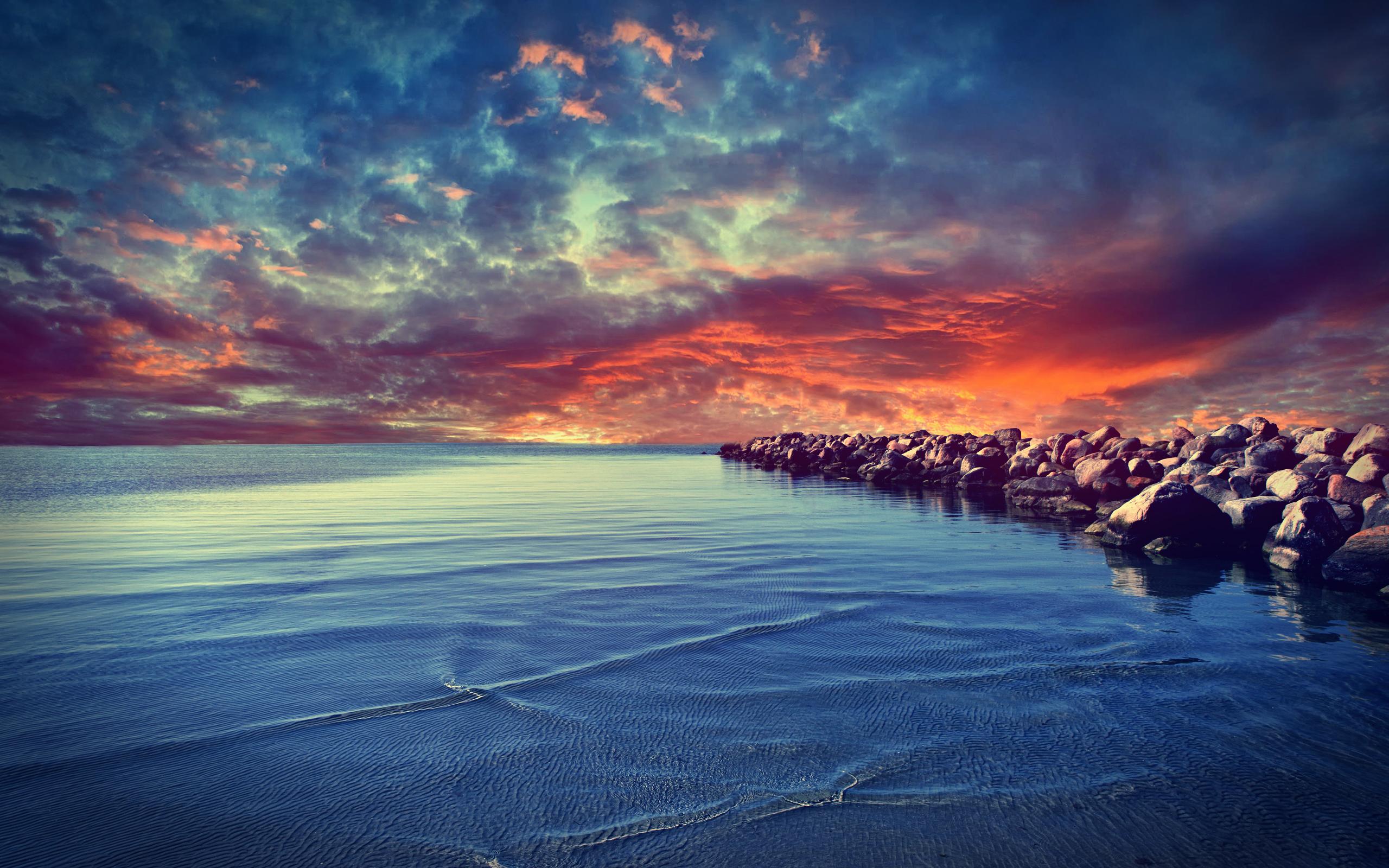 A breathtaking sunset over a tranquil ocean, with a rocky breakwater stretching into the water