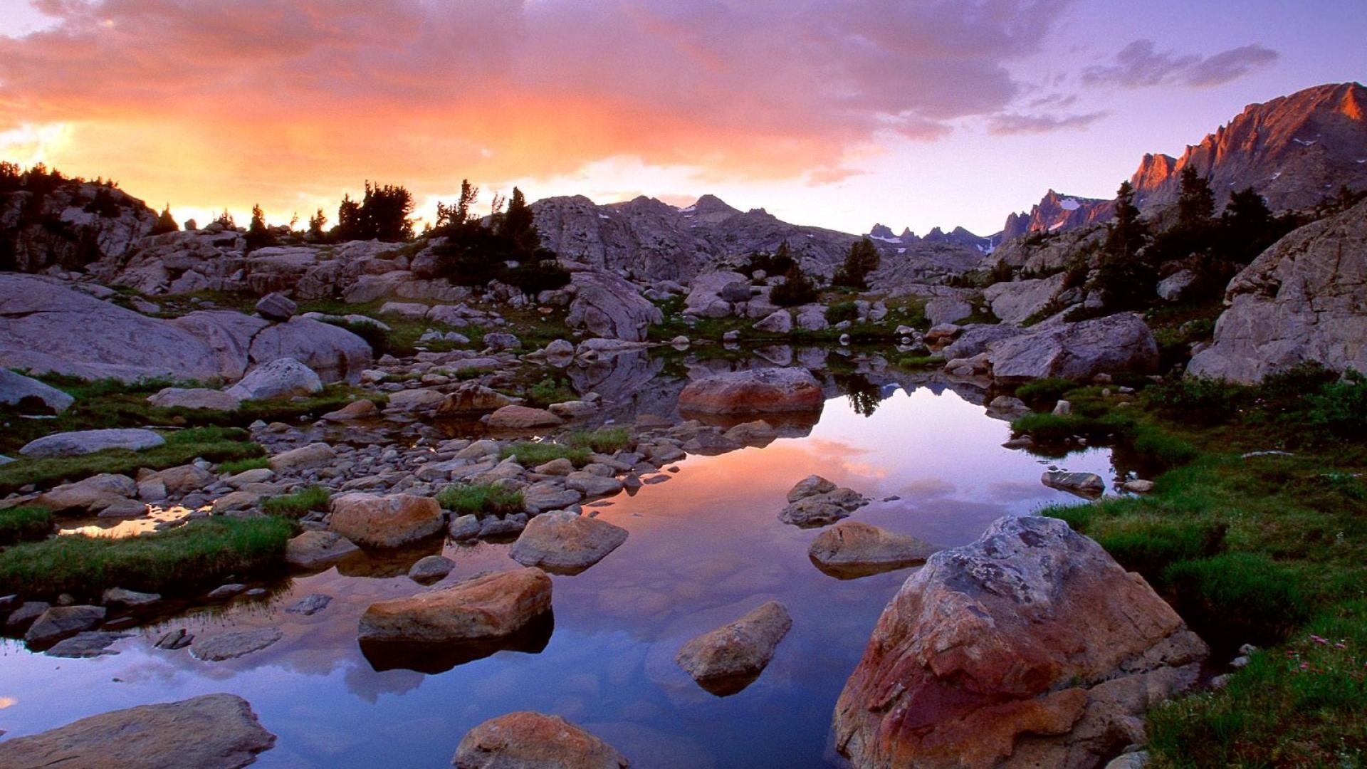 A serene sunset reflecting in a high-altitude alpine lake, surrounded by rugged rocks and sparse vegetation