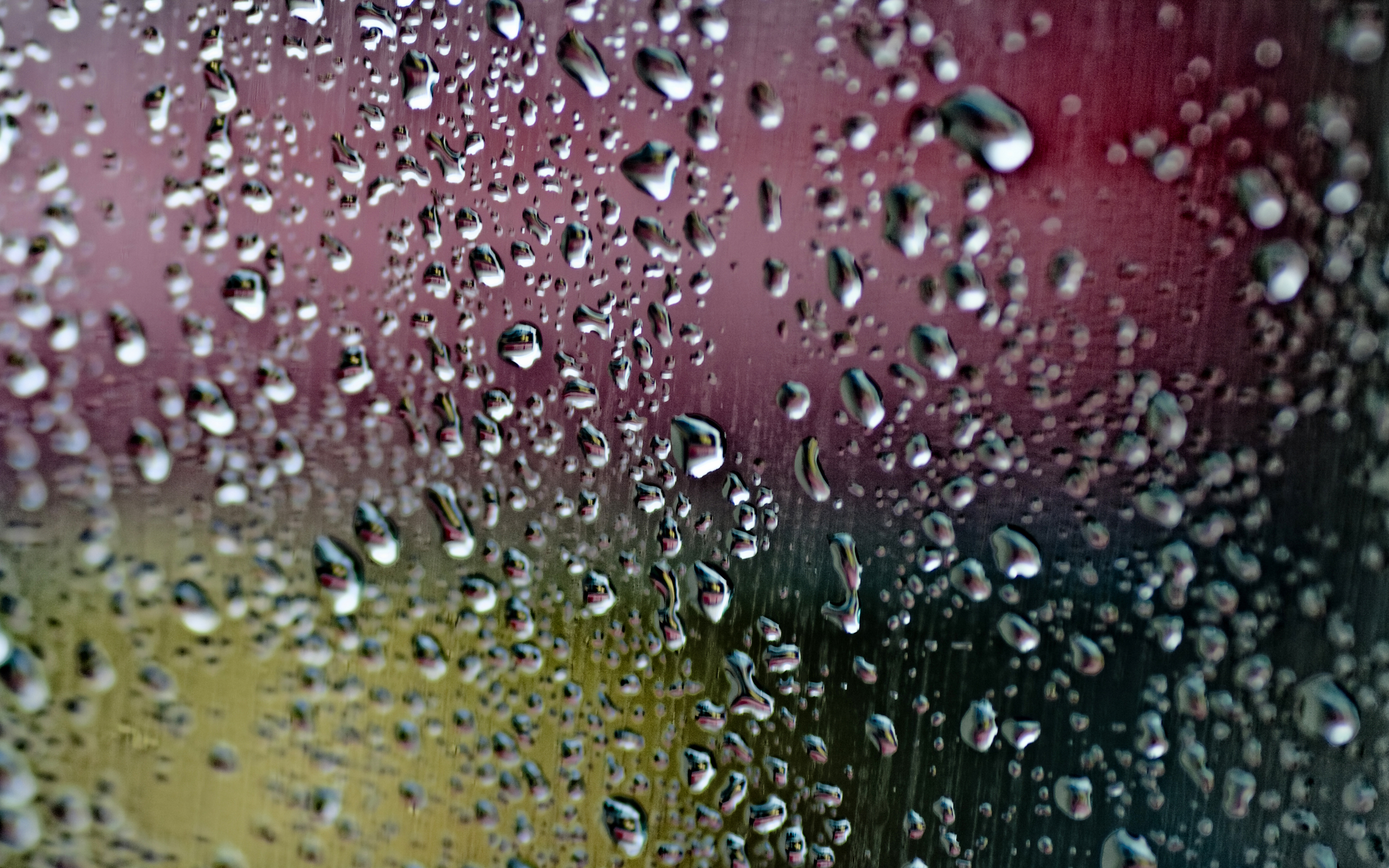 Close-up of raindrops clinging to a window pane, reflecting a blurred, multicolored background