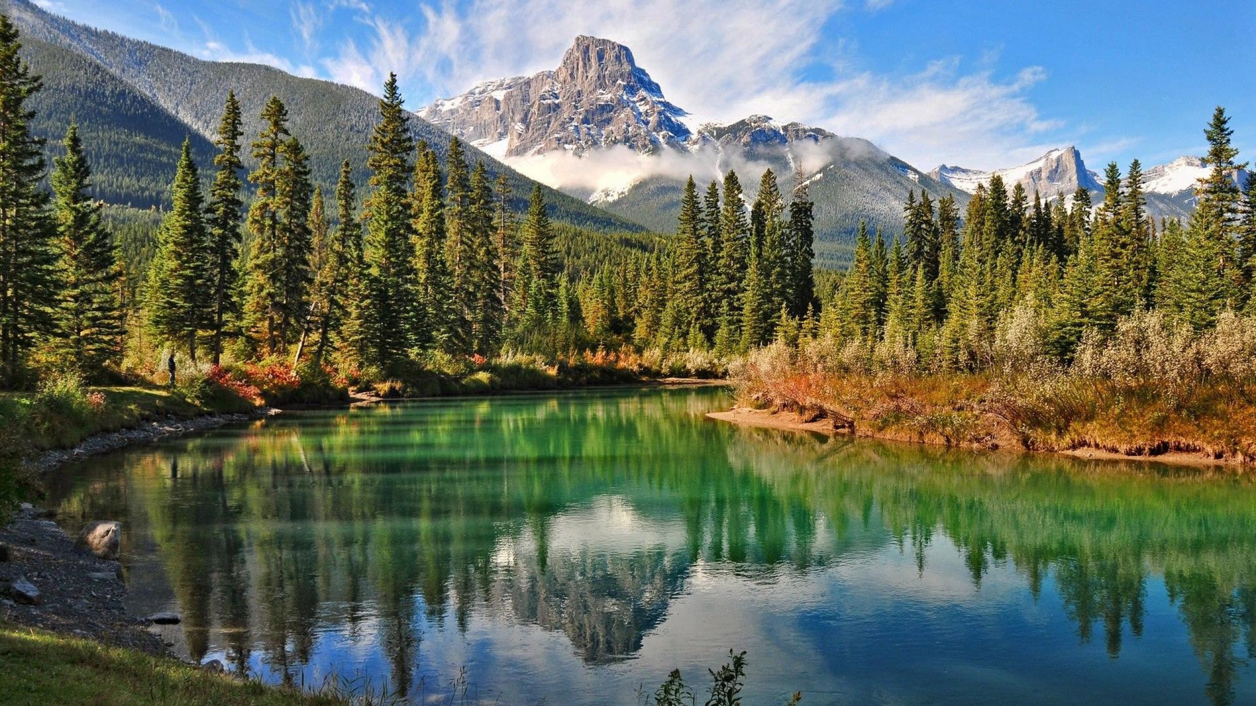 A serene lake reflecting a majestic mountain peak and a lush forest in Banff National Park, Canada